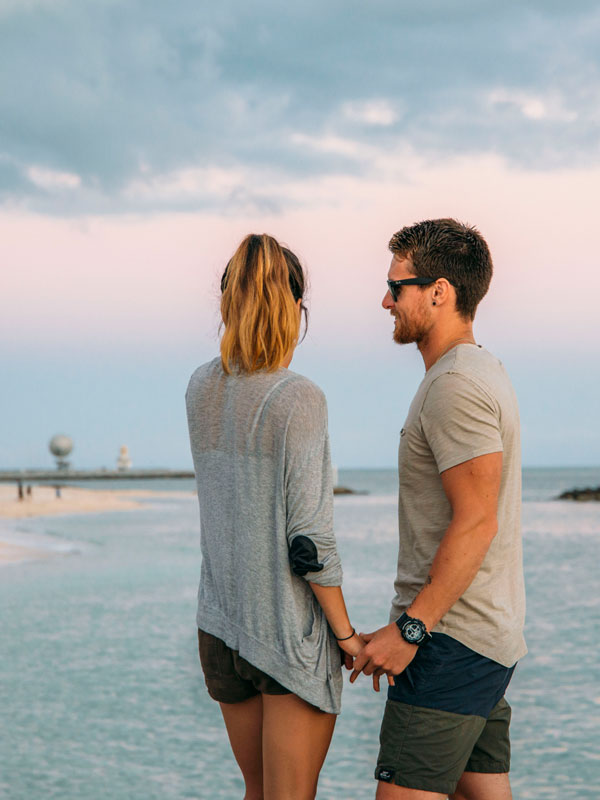 photo of a couple holding hands with the ocean and beach in the background.
